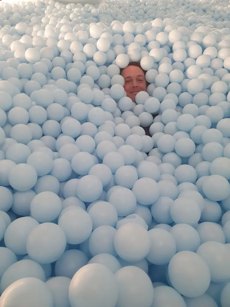 A visitor surrounded by pale blue balls at Color Factory